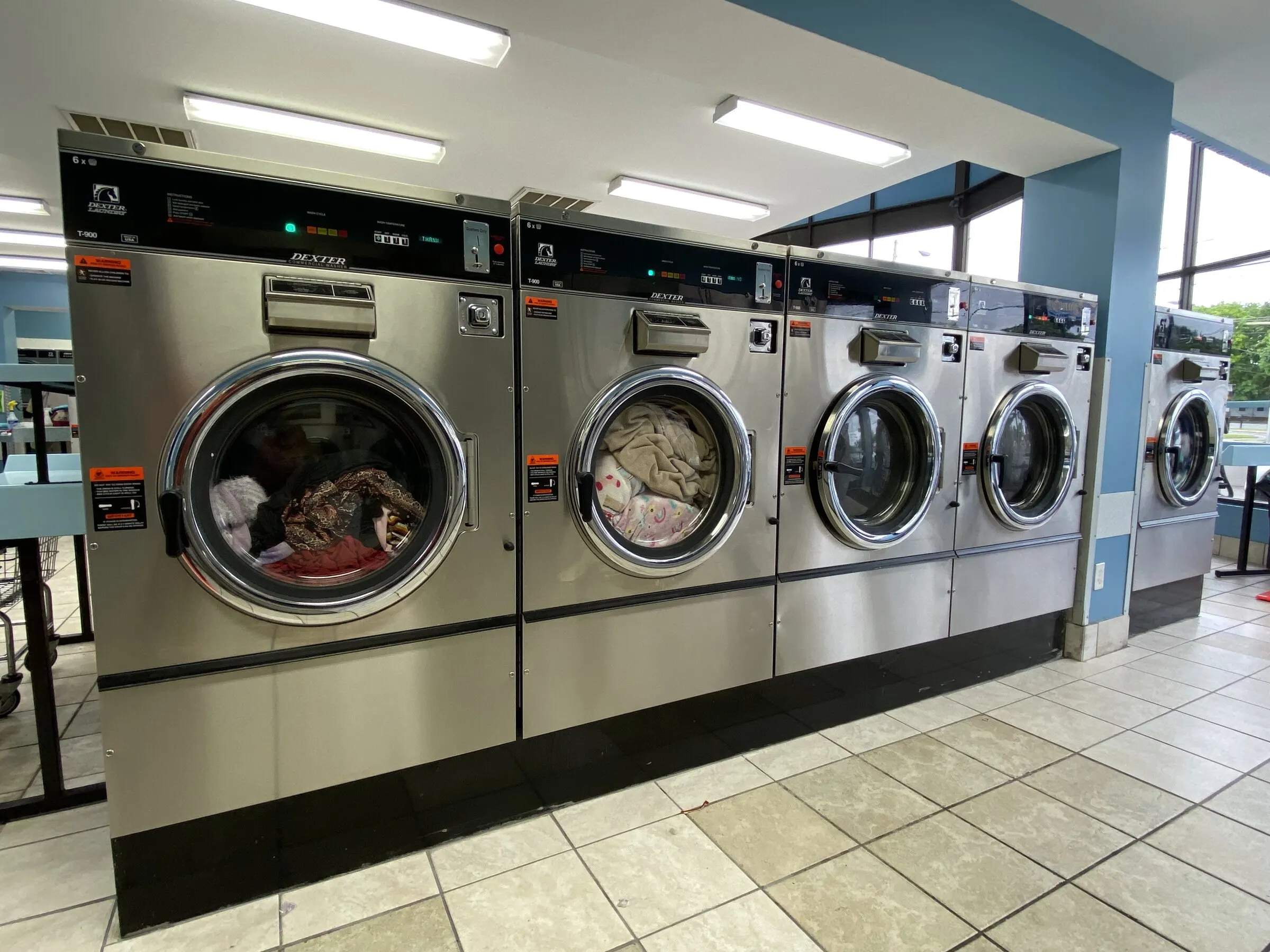Large washers running, a laundry cart at the left and a folding table in the background.