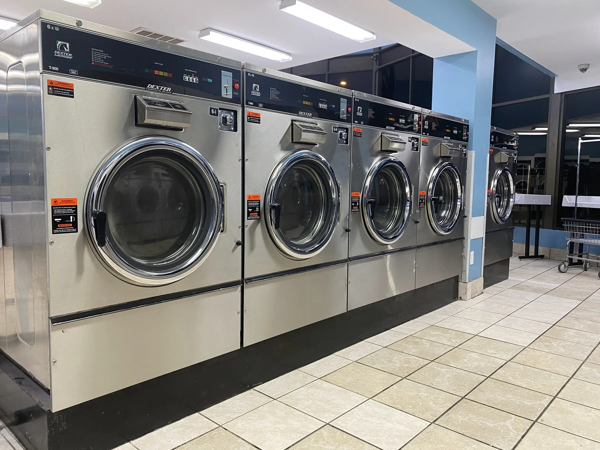 Five 60-pound washers with a laundry cart and folding table behind them.